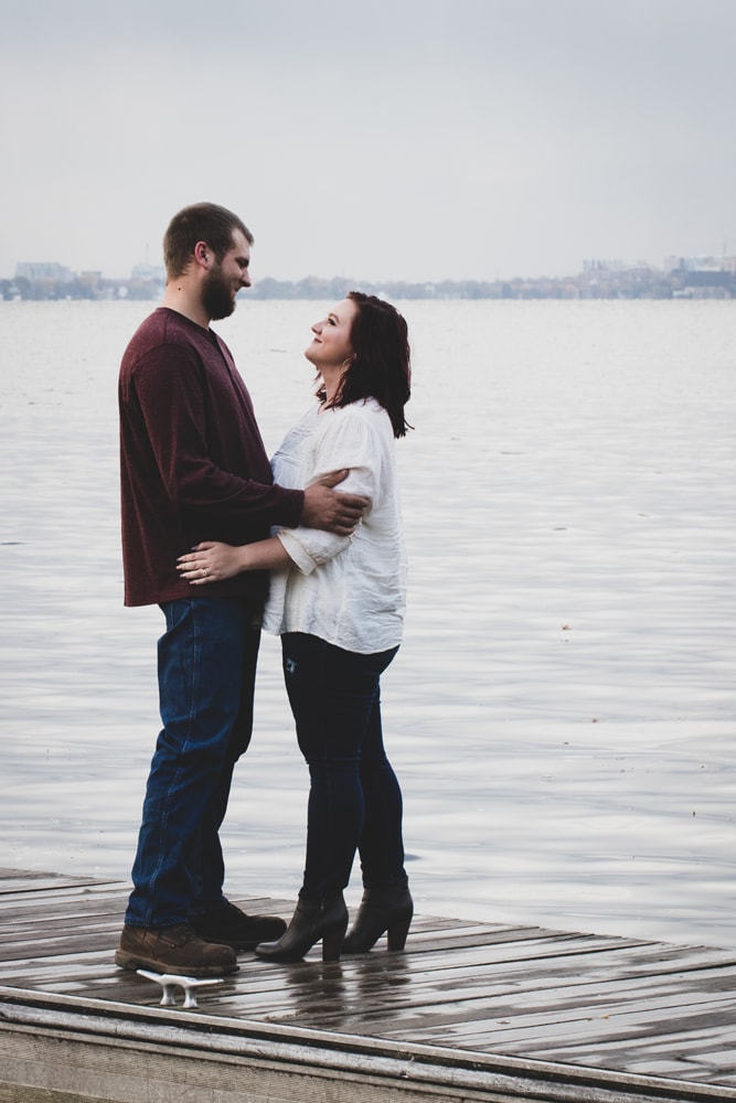 Romantic couple embracing on lakeside dock during intimate engagement session in Madison, Wisconsin