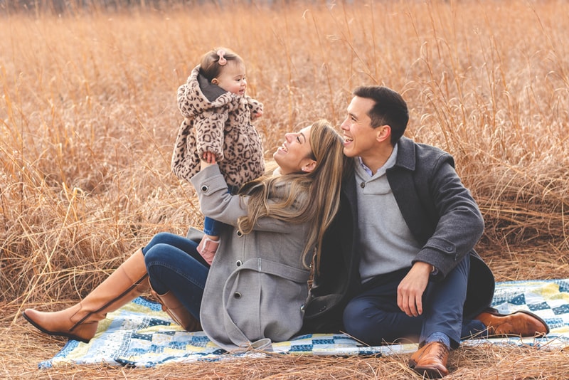 Joyful family of three laughing together on blanket in golden field during Madison, Wisconsin family portrait session