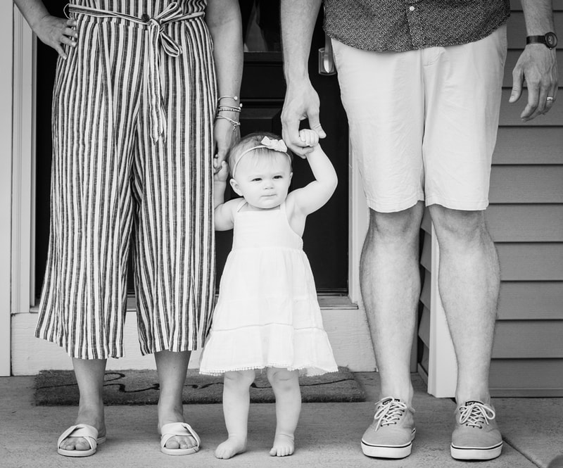 Joyful toddler between parents on front porch during family portrait session in Madison, Wisconsin