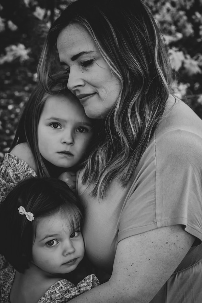 Mother tenderly embracing two young daughters in intimate black and white family portrait, Madison Wisconsin