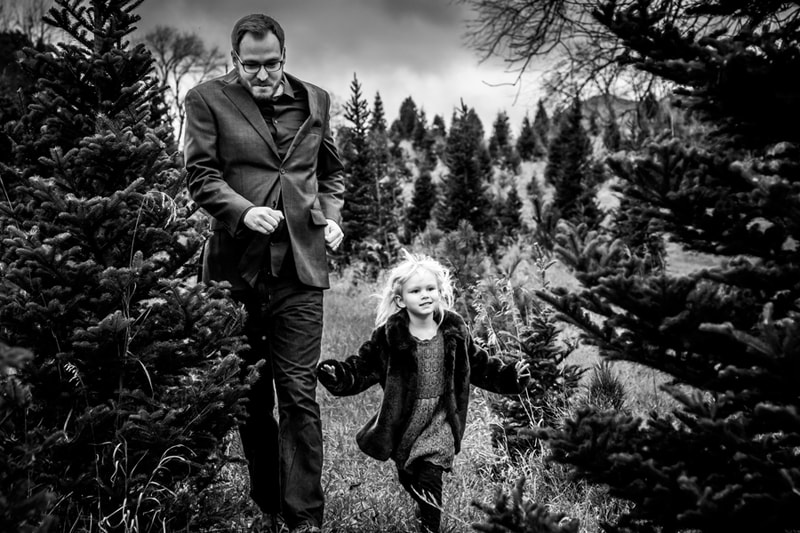 Father and daughter walking hand-in-hand through evergreen trees, joyful family portrait session in Madison, Wisconsin