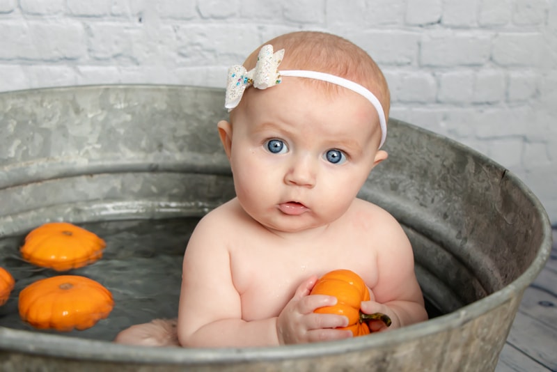 Baby girl with white flower headband sits in vintage tub with oranges, Madison Wisconsin family portrait session.