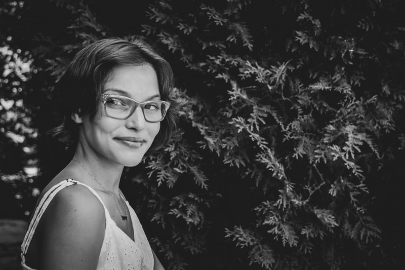 Young woman with glasses smiling warmly against lush foliage backdrop in Madison, Wisconsin family portrait