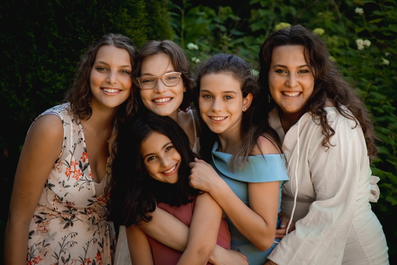 Joyful family portrait featuring five sisters embracing outdoors in lush Madison, Wisconsin greenery