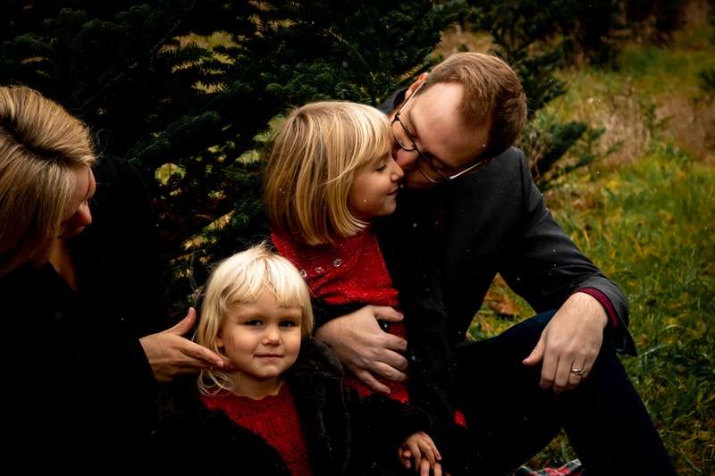 Father tenderly embraces young daughter while family gathers for intimate portrait session in Madison, Wisconsin