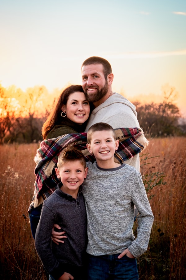 Joyful family of four embracing in golden prairie field during sunset family portrait session in Madison, Wisconsin
