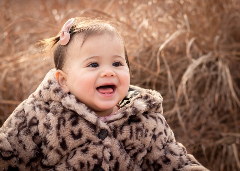Joyful toddler in leopard print coat smiling outdoors during Madison Wisconsin family portrait session