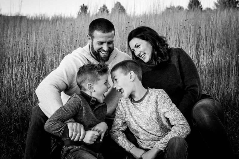 Joyful family of four laughing together in tall grass field during Madison, Wisconsin family portrait session