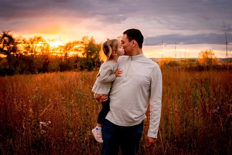 Father holding toddler in golden sunset field, intimate family portrait session in Madison, Wisconsin