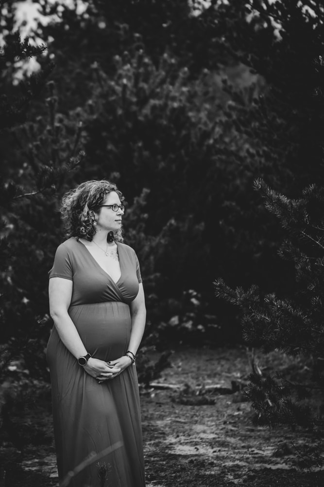 Expecting mother in flowing dress poses serenely among trees during Madison, Wisconsin maternity photography session