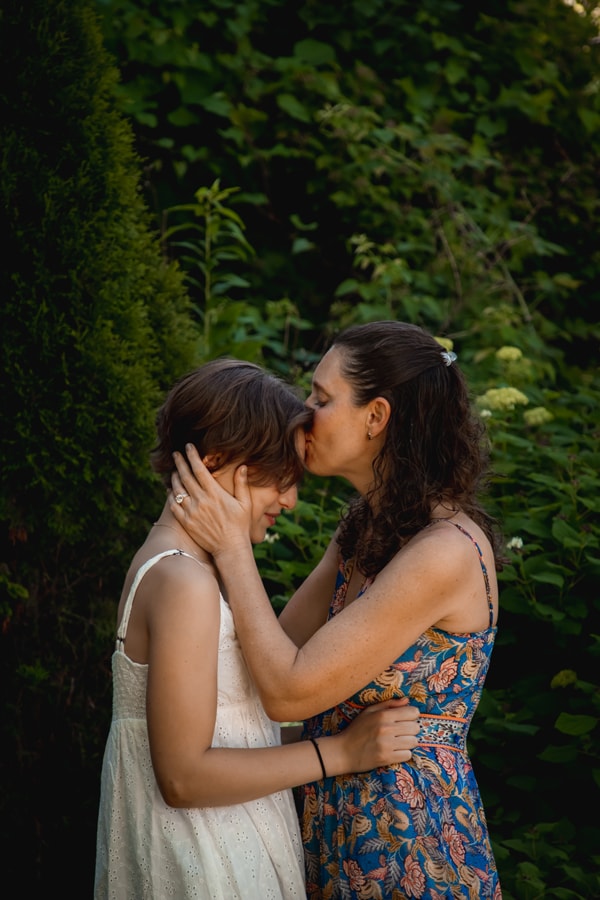 Mother tenderly kisses daughter's forehead in lush garden setting, Madison Wisconsin family photography session