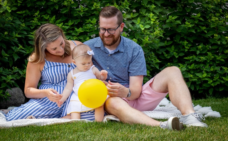 Joyful family with toddler playing with yellow ball during outdoor portrait session in Madison, Wisconsin