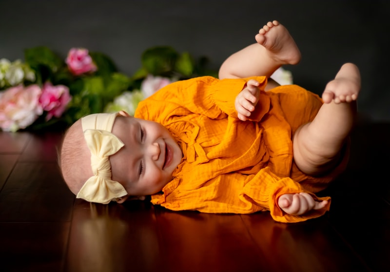 Joyful baby in orange outfit laughing during milestone portrait session in Madison, Wisconsin