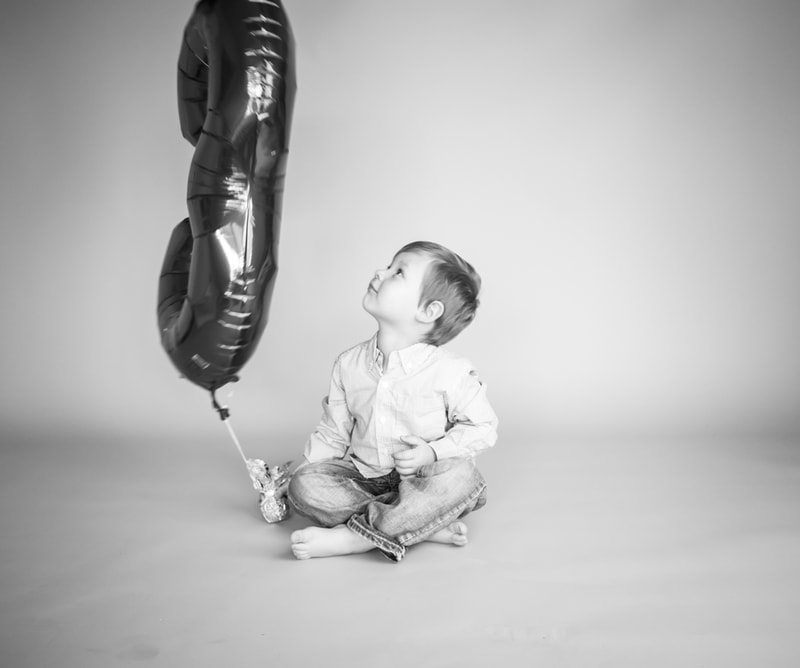 Joyful toddler gazing up at number balloons during milestone portrait session in Madison, Wisconsin