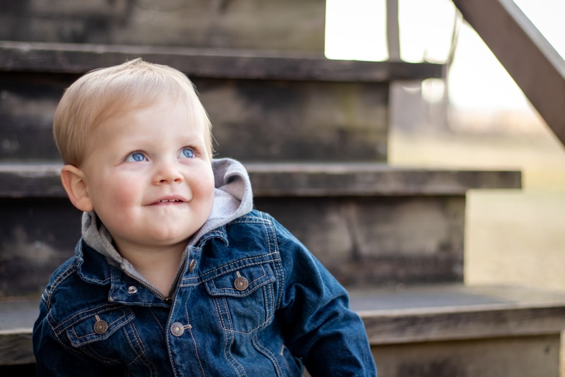 Blonde toddler in denim jacket smiling joyfully on wooden steps, milestone portrait session in Madison, Wisconsin