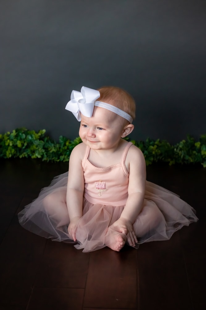 Joyful baby in pink tutu and white bow during milestone portrait session in Madison, Wisconsin