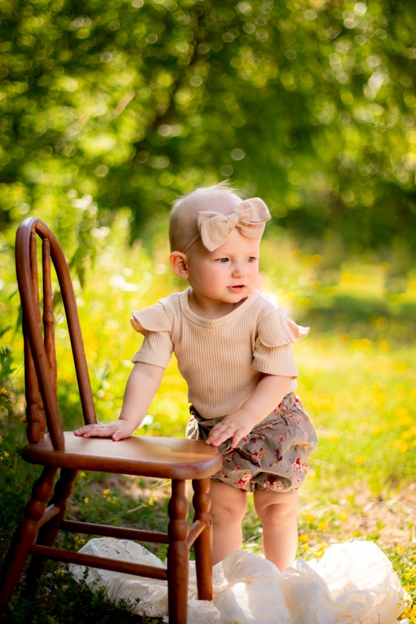 Sweet toddler girl standing on wooden chair during golden hour milestone portrait session in Madison, Wisconsin