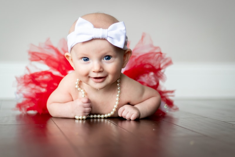 Smiling baby in red tutu and white bow celebrates milestone portrait session in Madison, Wisconsin