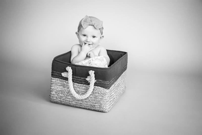 Smiling baby girl with bow headband sitting in woven basket during milestone photography session in Madison, Wisconsin