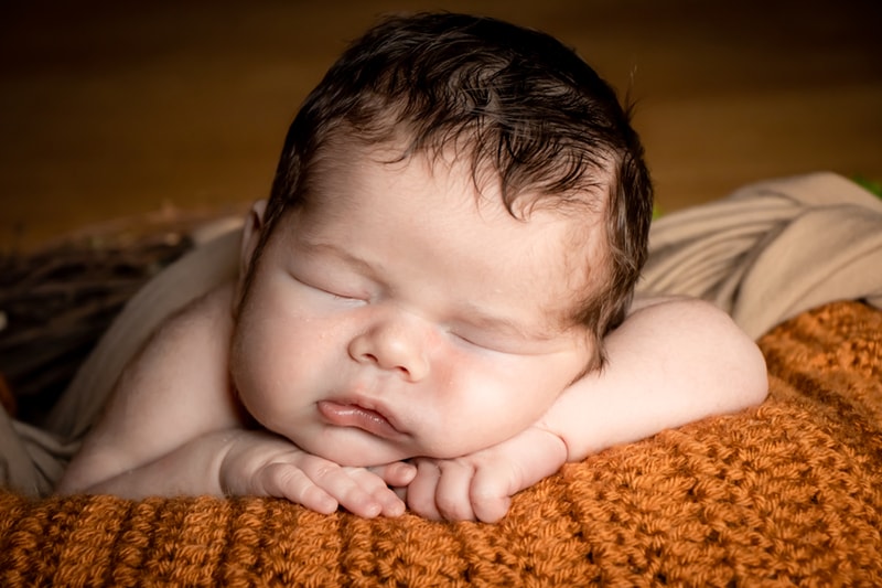 Peaceful sleeping newborn with dark hair resting on orange knit blanket during Madison Wisconsin portrait session