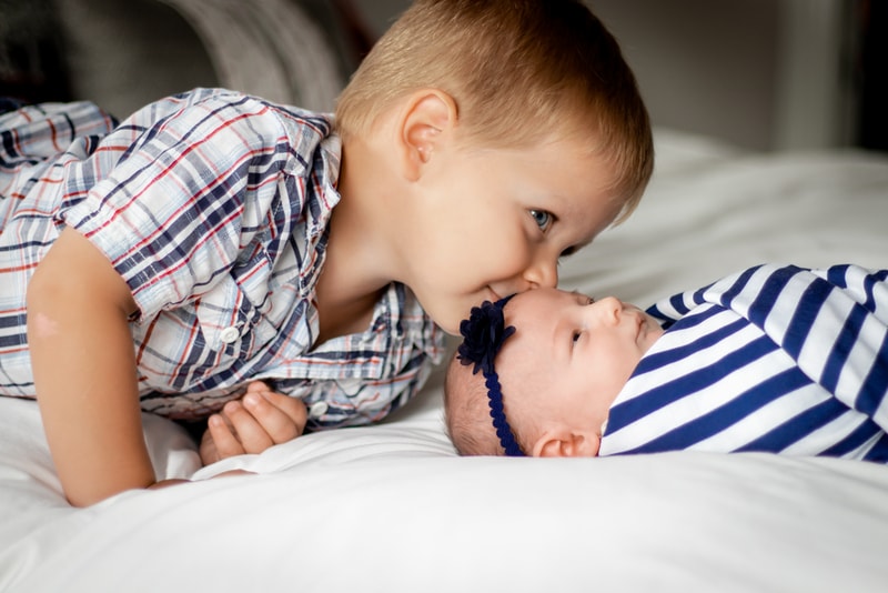 Tender sibling moment with toddler kissing newborn baby in Madison Wisconsin newborn portrait session