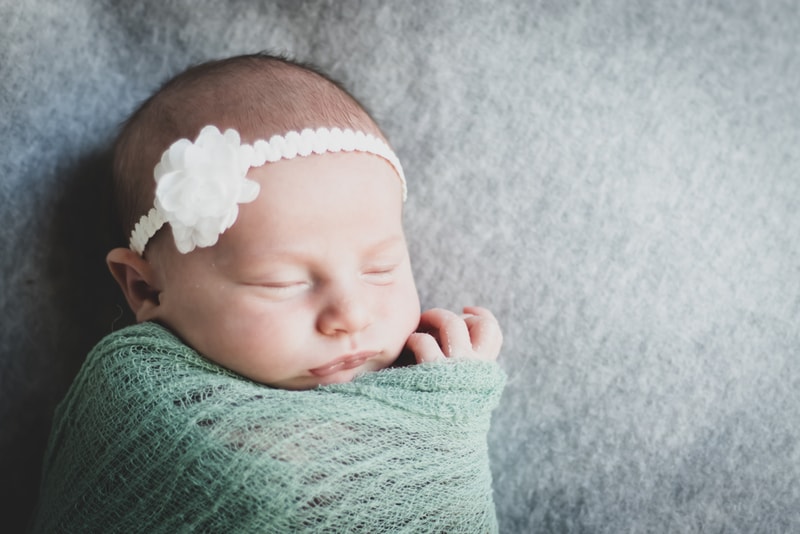 Peaceful sleeping newborn with white flower headband wrapped in sage green blanket, Madison Wisconsin newborn portrait