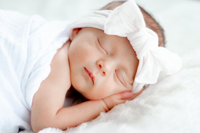 Peaceful sleeping newborn with white bow headband, serene newborn portrait photography in Madison, Wisconsin