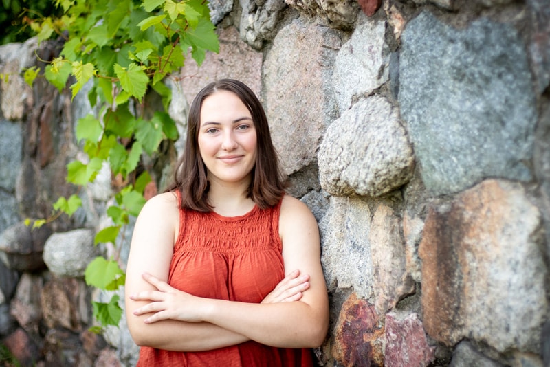 Confident senior poses against stone wall with green foliage in Madison, Wisconsin portrait session