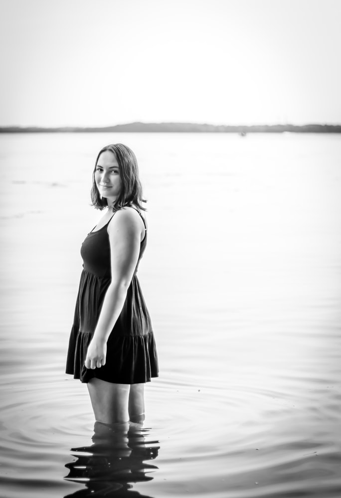 Confident high school senior in black dress wading in lake water, Madison Wisconsin senior portrait photography